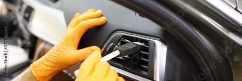 Master repairman in rubber gloves cleaning car air conditioner with brush in workshop closeup photo