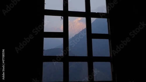 Mysterious snowy mountains peaks in pink dawn, view from black murk window frame