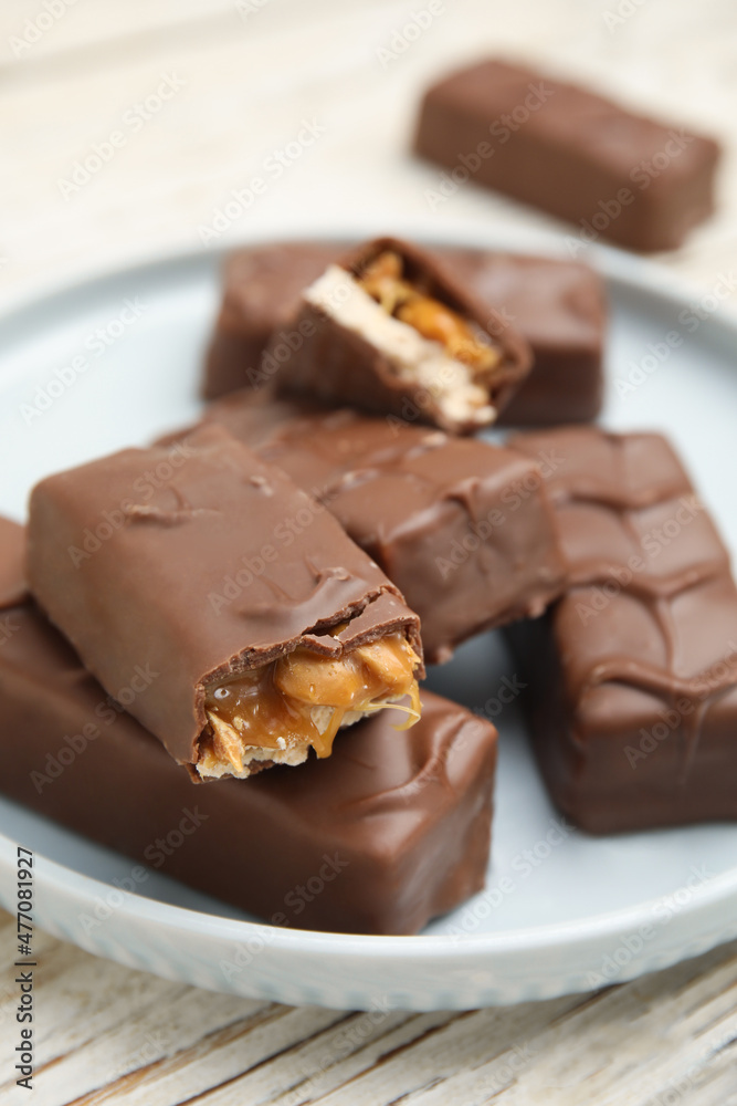 Plate of chocolate bars with caramel, nuts and nougat on white wooden table, closeup