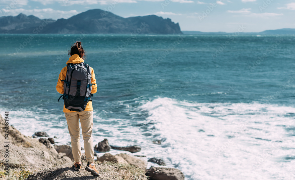Tourist with a backpack against the sea, panorama. Portrait of a woman in tourist gear against the sea. Travel and active lifestyle concept. Portrait of a traveler in a yellow jacket. Copy space
