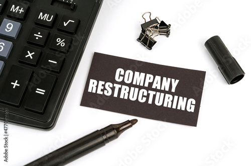 On a white table there is a calculator, a marker and a black plate with the inscription - Company Restructuring