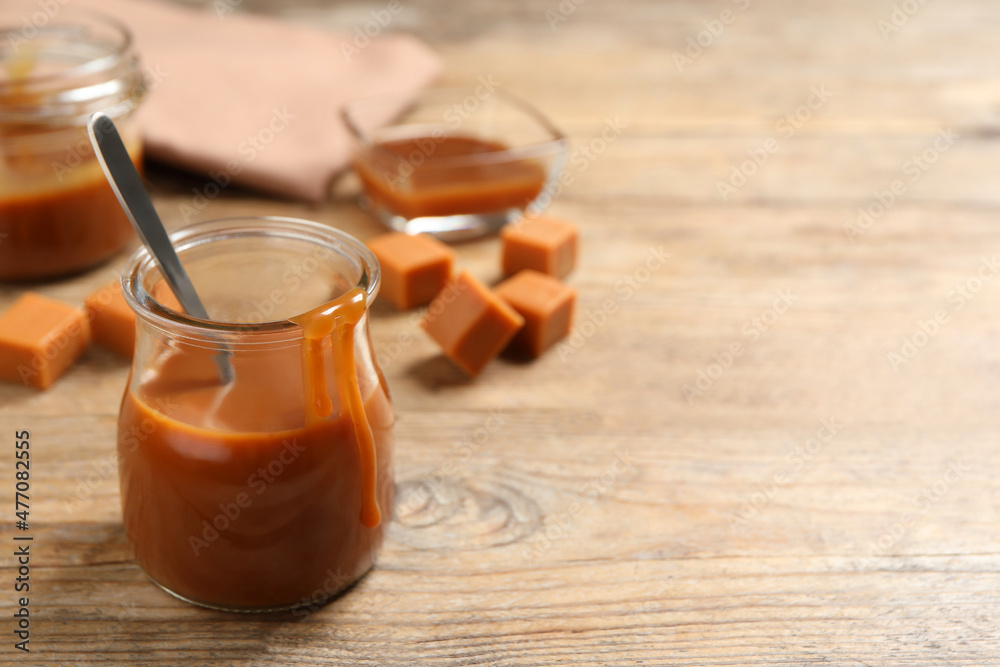 Tasty salted caramel and spoon in glass jar on wooden table, space for text Tasty salted caramel and spoon in glass jar on wooden table, space for text