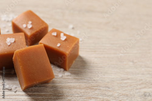 Tasty caramel candies and sea salt on light wooden table, closeup. Space for text