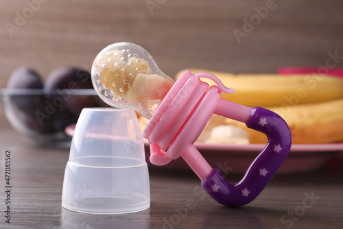 Nibbler with fresh banana on wooden table, closeup. Baby feeder photo