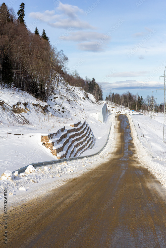 Winter road in the mountains, traveling through snowy mountainous terrain on a sunny frosty day.