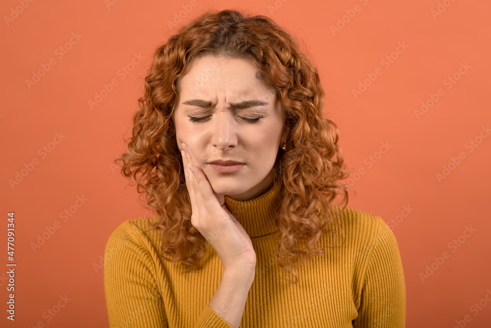 Young and attractive caucasian redhead girl touching her mouth with toothache isolated on orange studio background. Young and attractive caucasian redhead girl touching her mouth with toothache isolated on orange studio background.