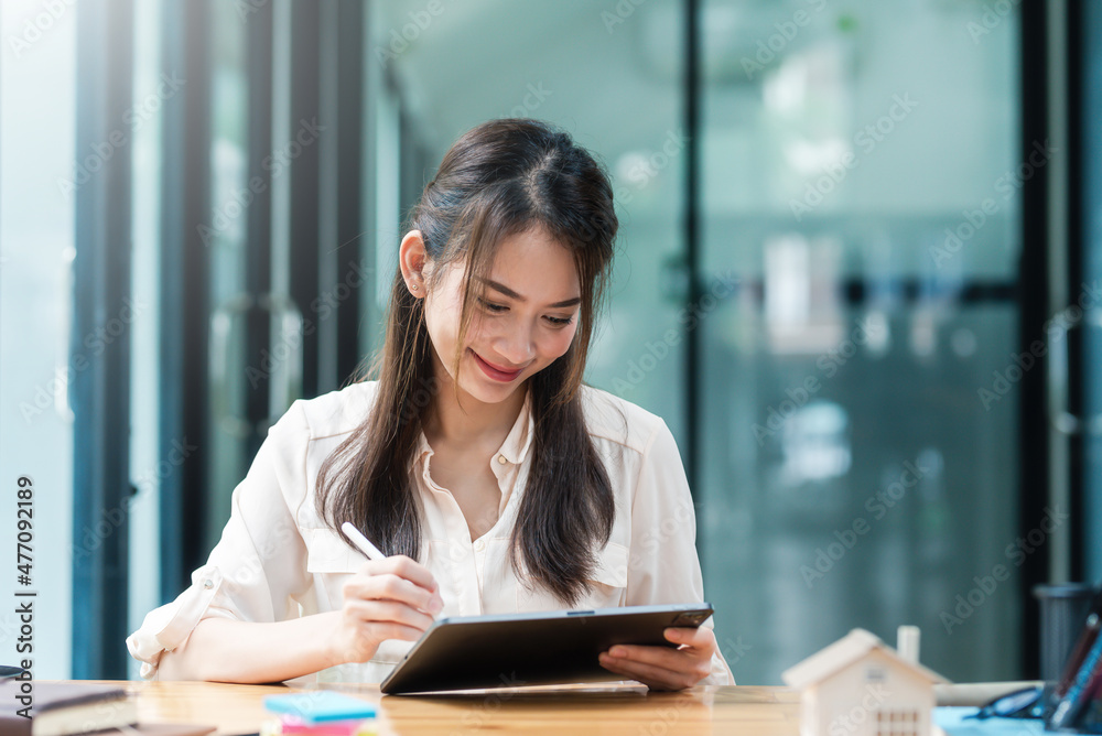 Portrait of smiling beautiful Asian businesswoman sitting enjoy the idea with tablet and laptop at office..