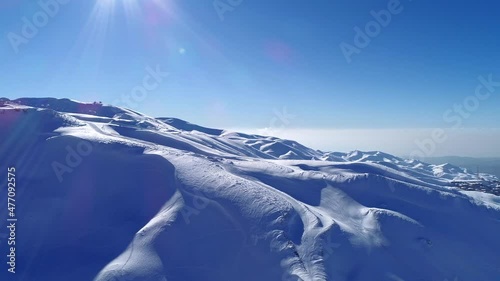 Aerial winter view with mountains covered by snow. Sunny day. Mountain peak with ski slopes. Freezing weather