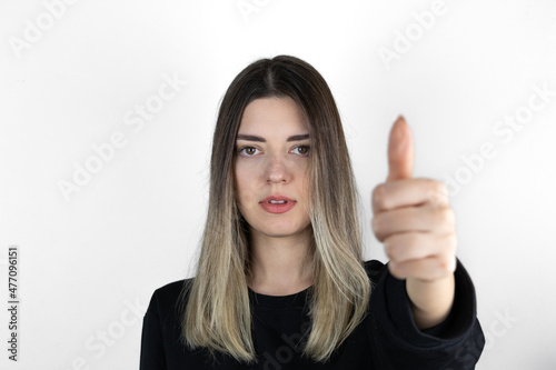 Young girl giving thumbs up. Girl with no emotions posing with thumbs up looking at camera. White studio background. The focus is on her hand. 