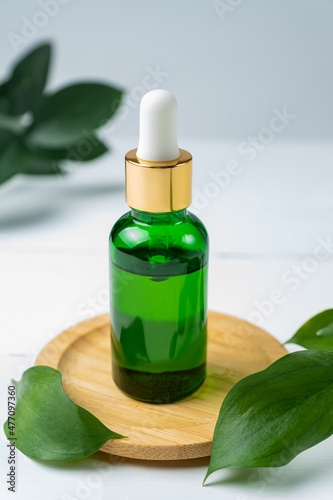 Green glass cosmetic bottle with a dropper on a white background with tropical leaves. Natural cosmetics concept  natural essential oil and skin care products