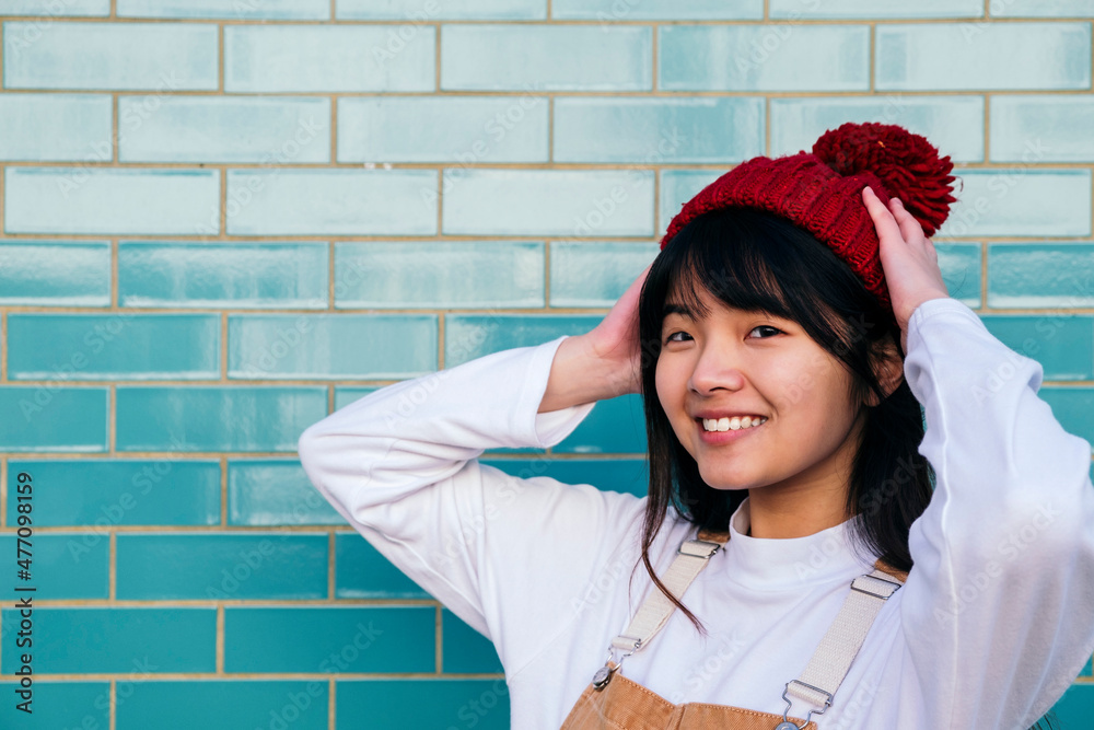 Smiling woman adjusting knit hat in front of turquoise wall Smiling woman adjusting knit hat in front of turquoise wall
