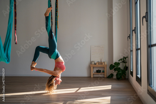 Woman hanging upside down on aerial silk practicing yoga at health club photo