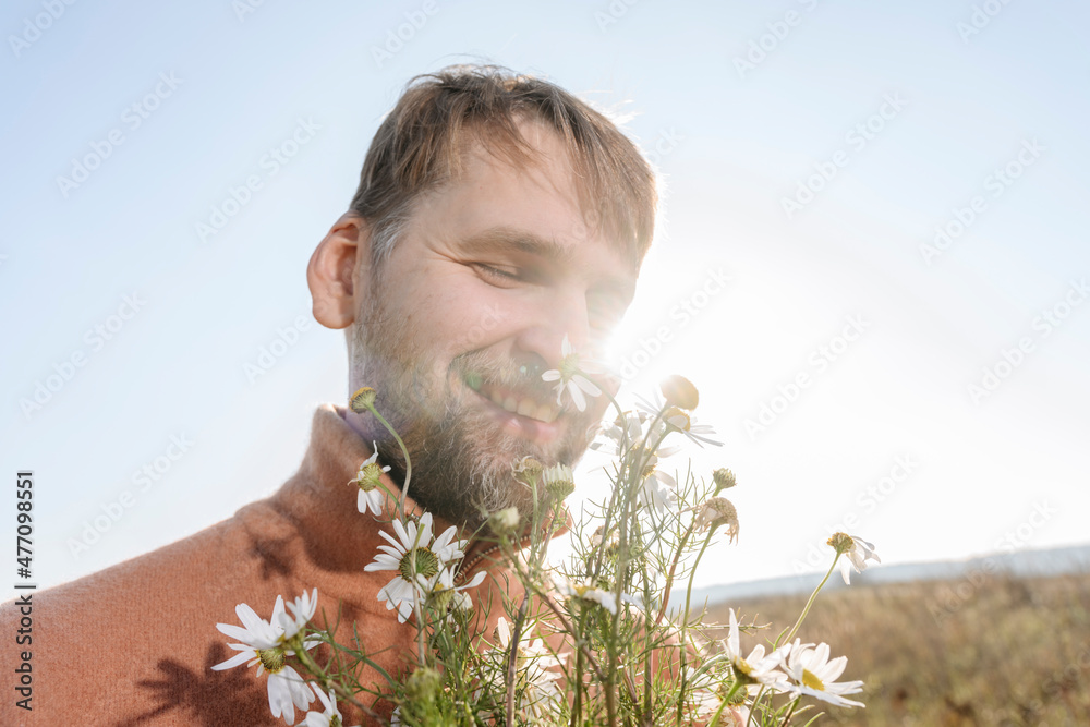 Smiling bearded man smelling chamomile flowers Smiling bearded man smelling chamomile flowers