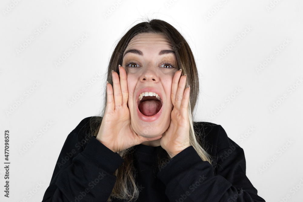 Announcing good news. Cheerful young girl holding hands around mouth and shouting while standing against white background. Crazy. Announcing good news. Cheerful young girl holding hands around mouth and shouting while standing against white background. Crazy.