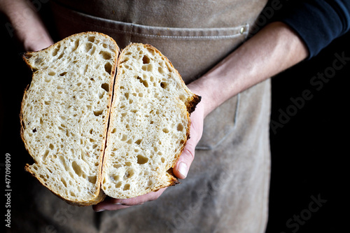 Baker holding halved loaf of bread at bakery photo