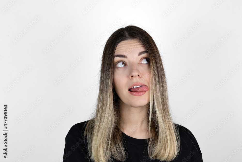 Young woman sticking out tounge, close up portrait. Teasing you through camera while isolated with white background. Young woman sticking out tounge, close up portrait. Teasing you through camera while isolated with white background.