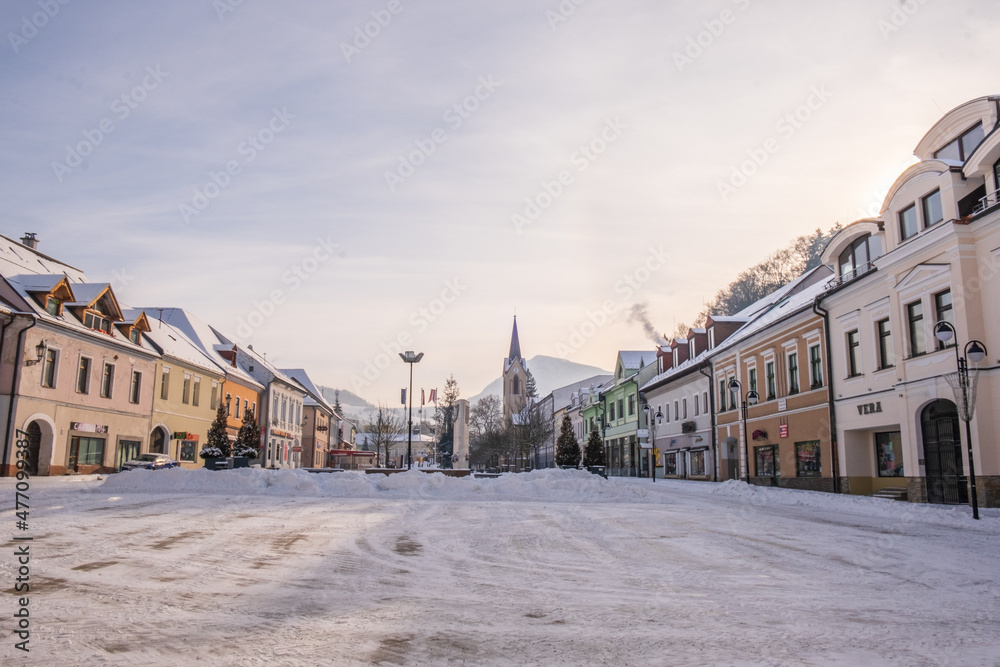 Fototapeta premium Dolny Kubin, Slovakia - December 26 2021: City centre of Dolny Kubin during Christmas time. Hviezdoslavov Square with towers of local churches. Snowy landscape and historic houses. Orava region