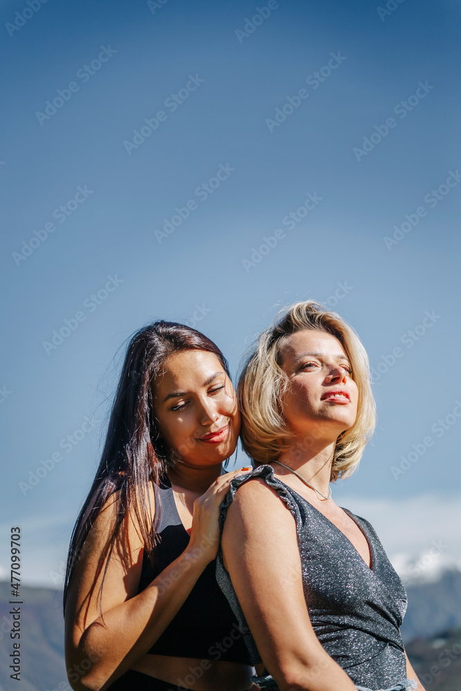 Young woman standing with blond friend under blue sky on sunny day Young woman standing with blond friend under blue sky on sunny day