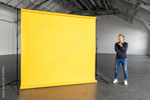 Thoughtful businessman looking at blank yellow backdrop in industial hall photo