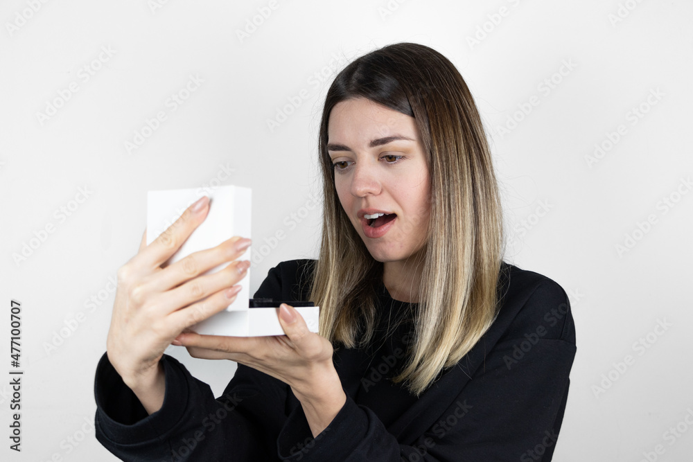 Girl is holding a small white box in her hand. When she sees the gift, she is happy and surprised. Girl is holding a small white box in her hand. When she sees the gift, she is happy and surprised.