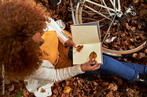 Woman with bicycle keeping leaf inside book sitting at autumn forest photo