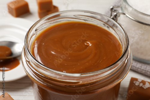 Yummy salted caramel in glass jar on table, closeup