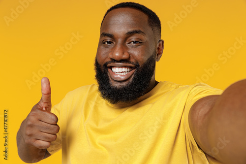 Close up young fun smiling happy black man 20s wearing bright casual t-shirt doing selfie shot pov on mobile phone isolated on plain yellow color background studio portrait. People lifestyle concept.