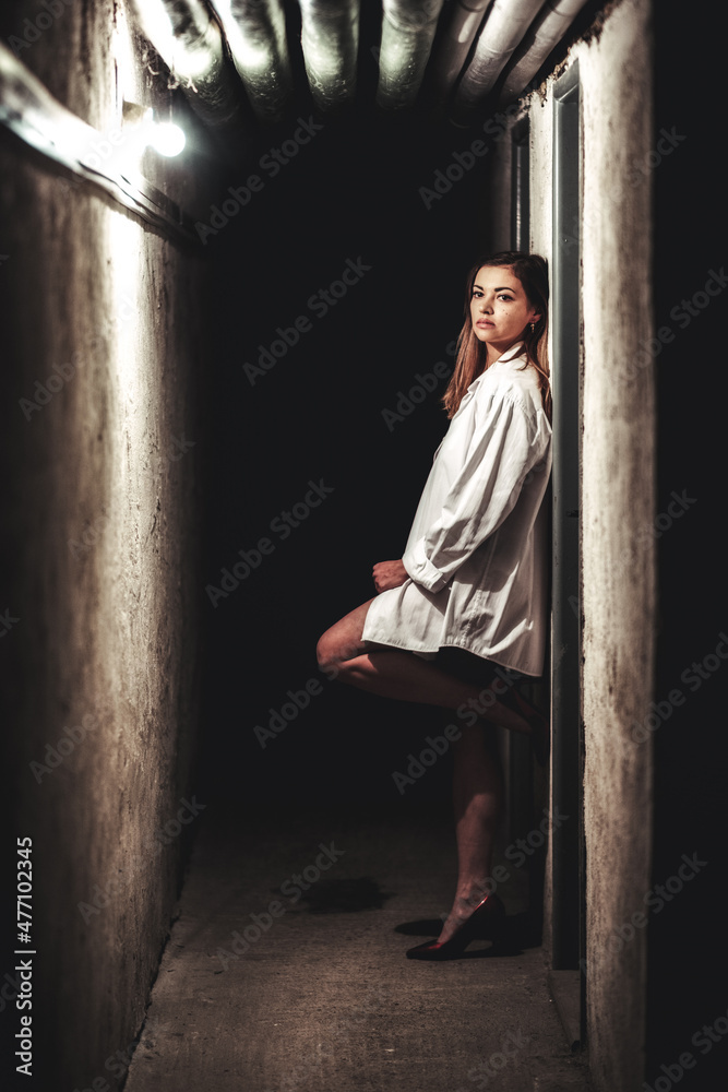 Girl in long white shirt with depressive expresion in dark hallway