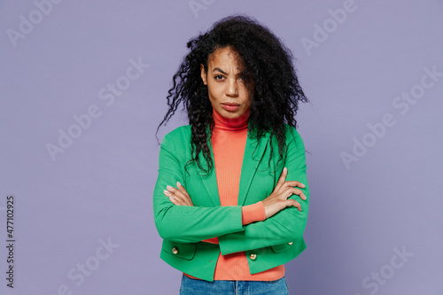 Frowning young black curly woman 20s years old wears green shirt looking camera hold hands crossed isolated on plain pastel light violet background studio portrait. People emotions lifestyle concept. © ViDi Studio