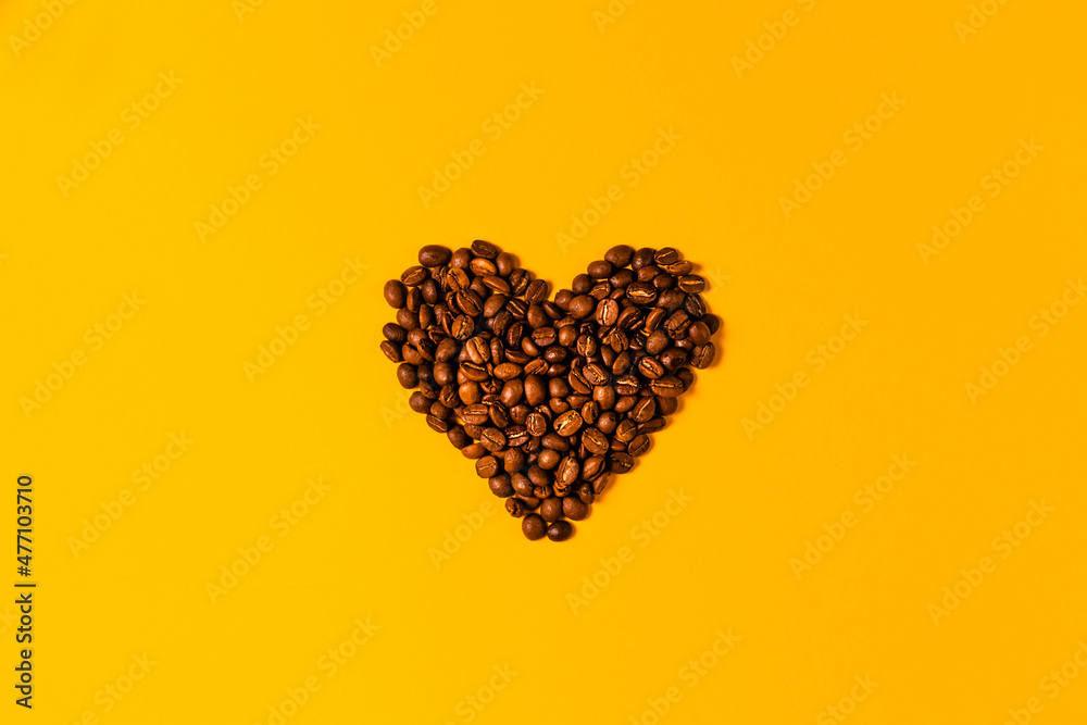 A stylish heart made of coffee beans on a yellow background. Freshly roasted Arabica seeds on a light background with space for text for your advertising A stylish heart made of coffee beans on a yellow background. Freshly roasted Arabica seeds on a light background with space for text for your advertising