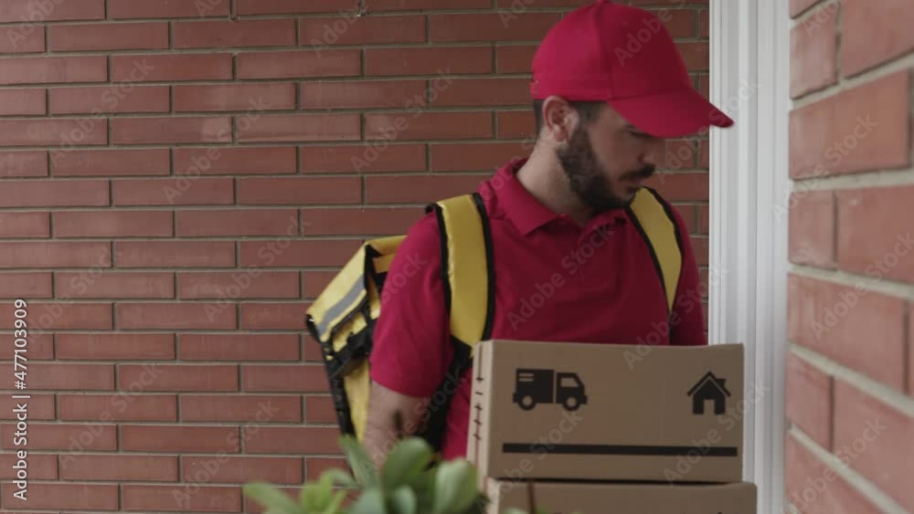 Delivery man in red uniform with thermal backpack ringing the house doorbell while holding cardboard box - Hispanic courier rider delivering a package - Small business and delivery service concept.