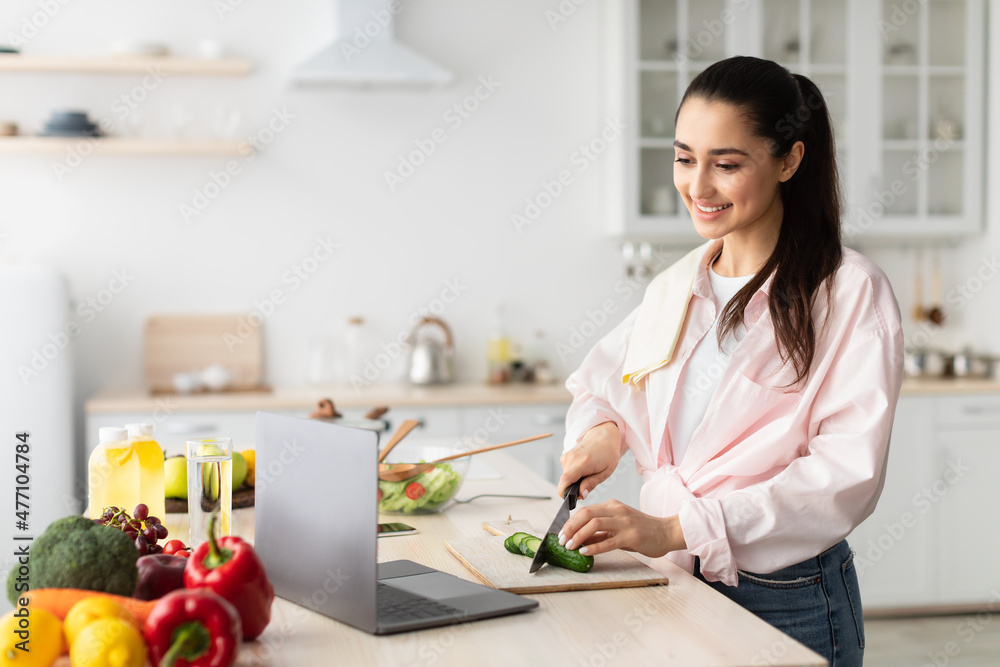 Woman cooking salad and using personal computer at kitchen