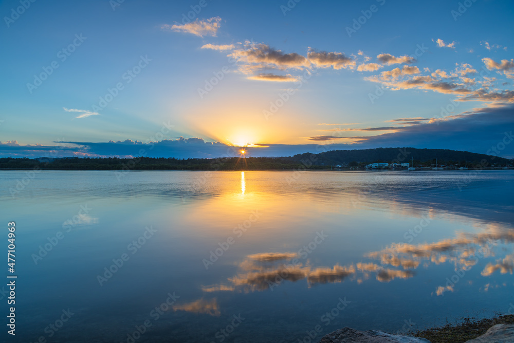 Sunrise waterscape with cloud reflections and sun rays