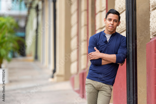 A portrait of a stylish young man standing in a city street, smiling, Panama city, Central America