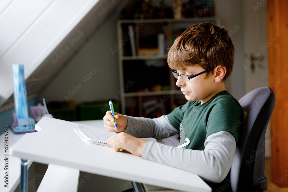 Kid boy with glasses learns at home for school. Preteen child making homework. Home schooling and distance learning concept.