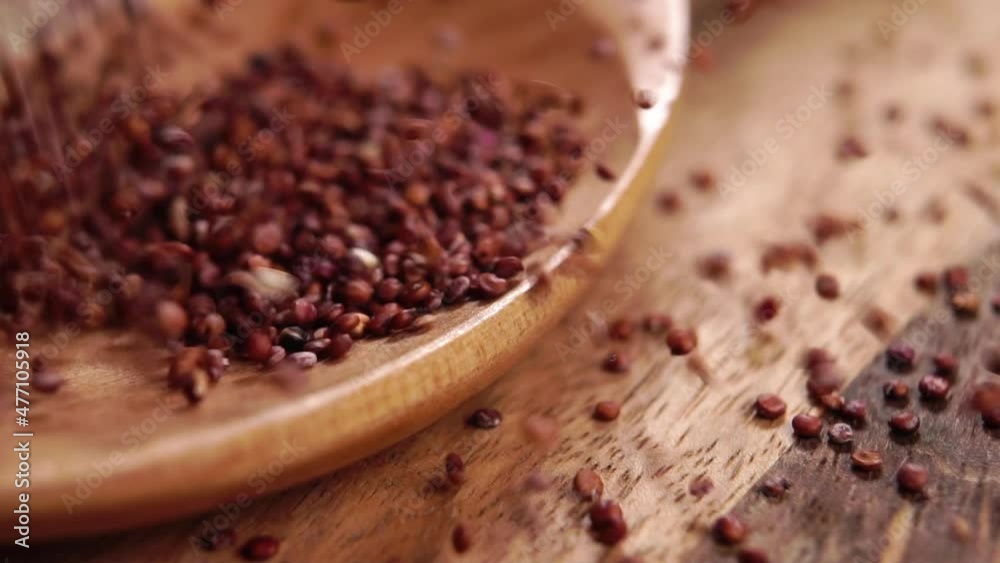 Falling raw red quinoa seeds into a rustic wooden spoon. Macro. Dry uncooked grains. Superfood concept Falling raw red quinoa seeds into a rustic wooden spoon. Macro. Dry uncooked grains. Superfood concept