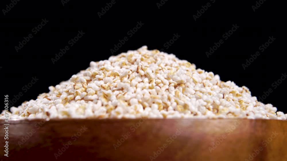 Puffed amaranth seeds in wooden bowl. Popped amaranthus grain on a black background. Macro. Turning