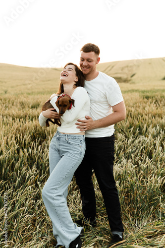 portrait of a young couple with a pet. the guy hugs the girl holding the dog. people in love walking along the field with a dog.lovers with a dog