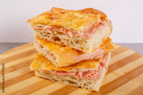 Tre pezzi di focaccia croccante ripiena di mortadella fresca sovrapposti a formare una piccola torre e poggiati su un tagliere di legno photo