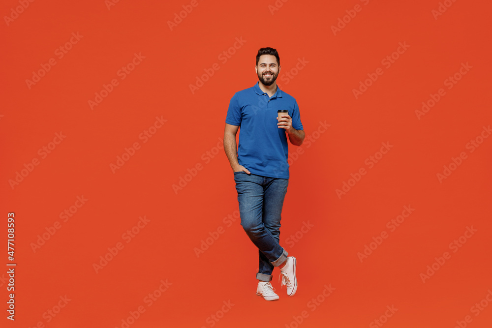 Full body young smiling happy man 20s wear basic blue t-shirt looking camera hold takeaway delivery craft paper brown cup coffee to go isolated on plain orange background. People lifestyle concept