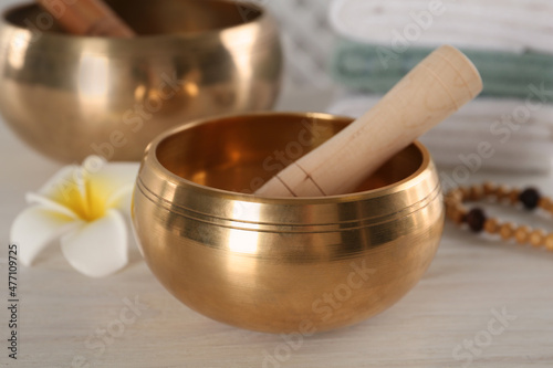 Golden singing bowl with mallet on white wooden table, closeup