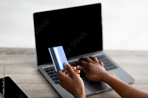 Distance shopping concept. Cropped view of black woman with credit card and laptop purchasing on web, mockup for website