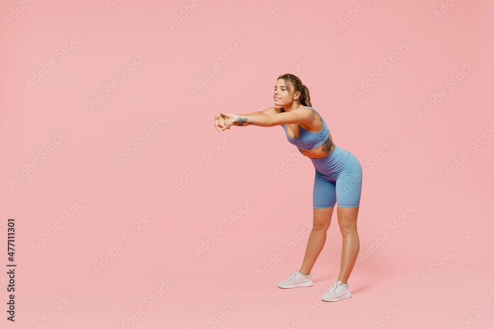 Full body young strong sporty athletic fitness trainer instructor woman 20s wear blue tracksuit spend time in home gym do squats isolated on pastel plain light pink background. Workout sport concept.