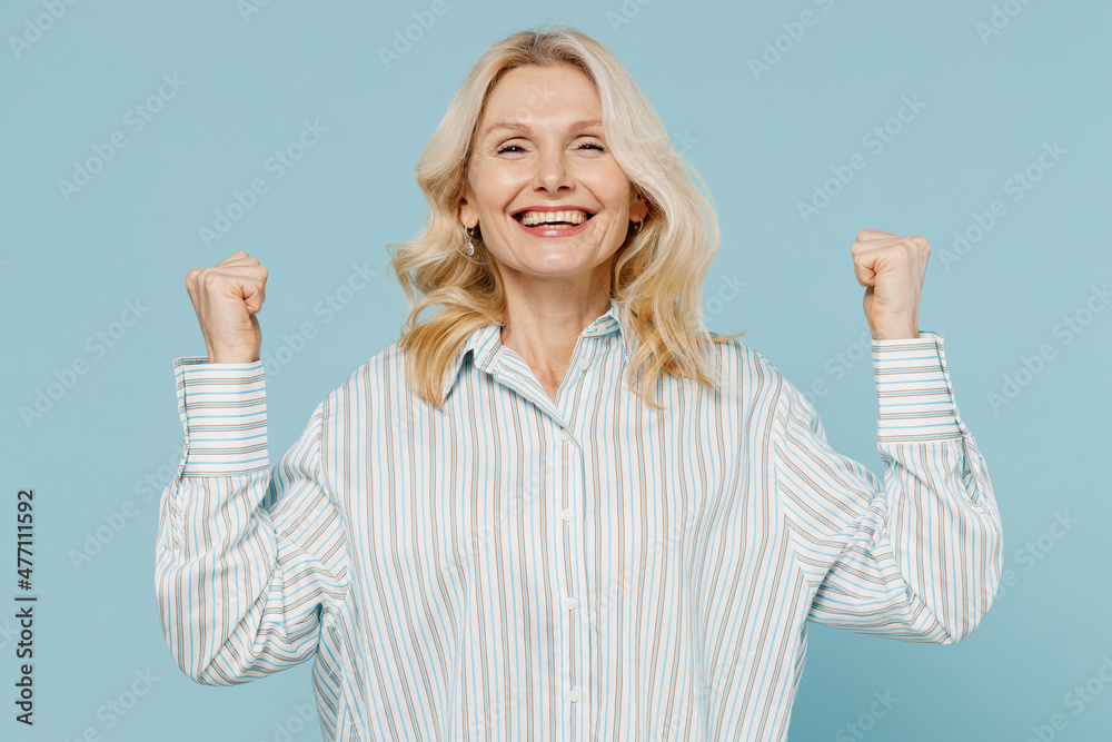 Elderly overjoyed excited fun cool caucasian woman 50s wear striped shirt do winner gesture clench fist isolated on plain pastel light blue color background studio portrait. People lifestyle concept. Elderly overjoyed excited fun cool caucasian woman 50s wear striped shirt do winner gesture clench fist isolated on plain pastel light blue color background studio portrait. People lifestyle concept.