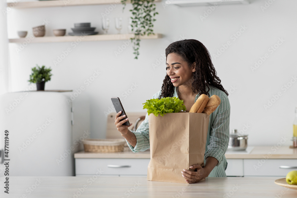 Delivering products to home. Smiling millennial african american female looks at smartphone