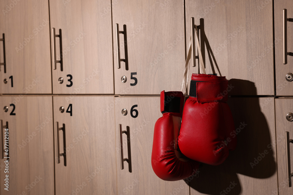 Red boxing gloves hanging on locker door in changing room. Space for text