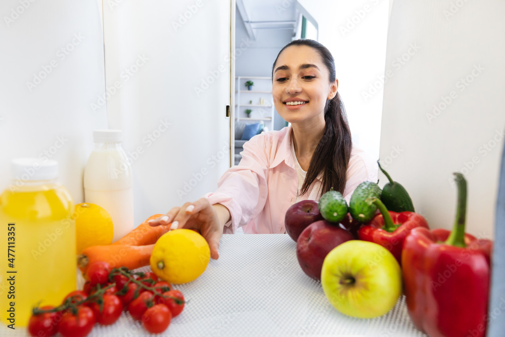 Smiling woman opening fridge and taking fresh food