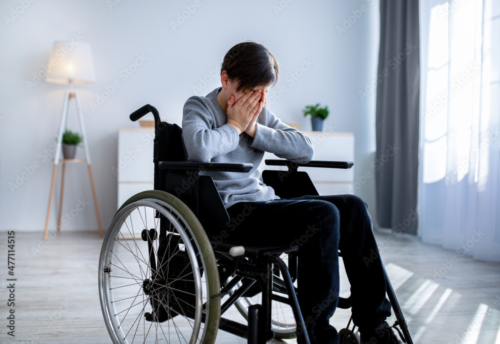 Depression in disabled teenagers. Unhappy handicapped teen boy in wheelchair crying at home Depression in disabled teenagers. Unhappy handicapped teen boy in wheelchair crying at home