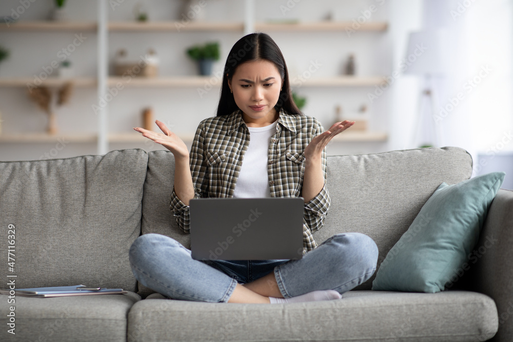 Puzzled asian lady looking at laptop screen, raising hands up Puzzled asian lady looking at laptop screen, raising hands up