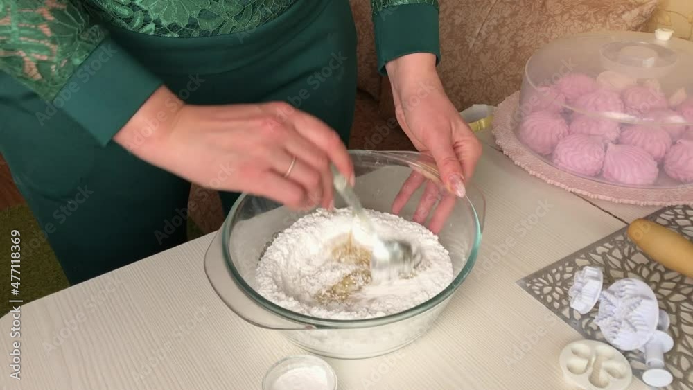 A woman is stirring honey and gelatin in powdered sugar. Makes pastry
